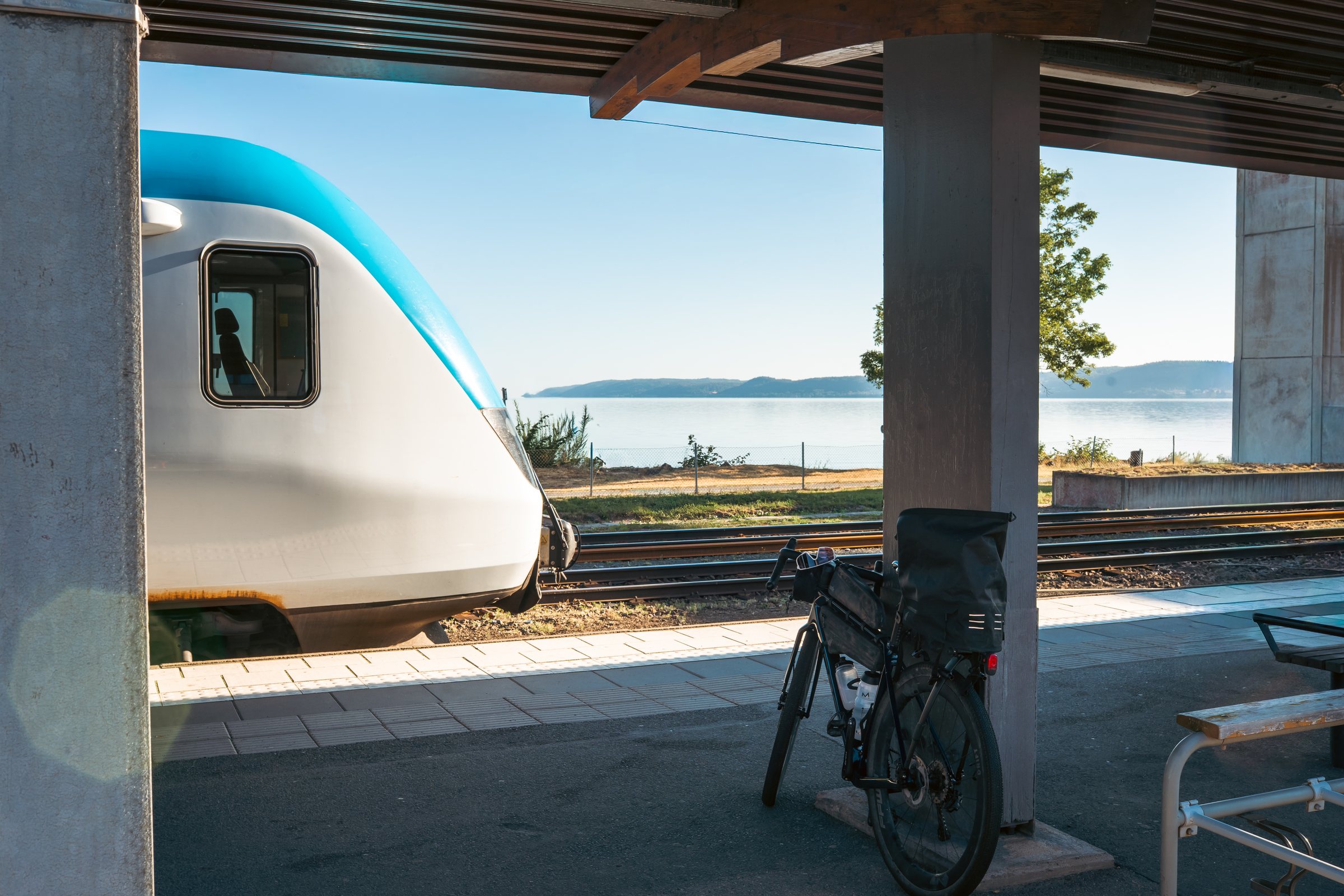 Loaded gravel bike parked on the platform at Jönköping station, train and Lake Vättern behind