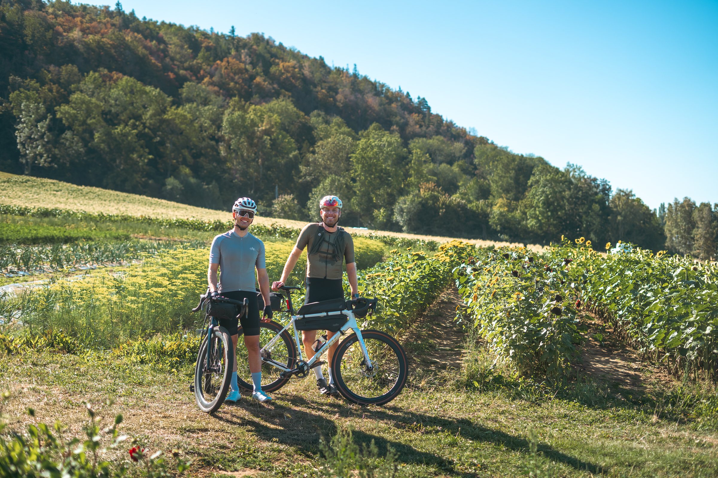 Two cyclists with loaded gravel bikes in a sunflower field above Huskvarna