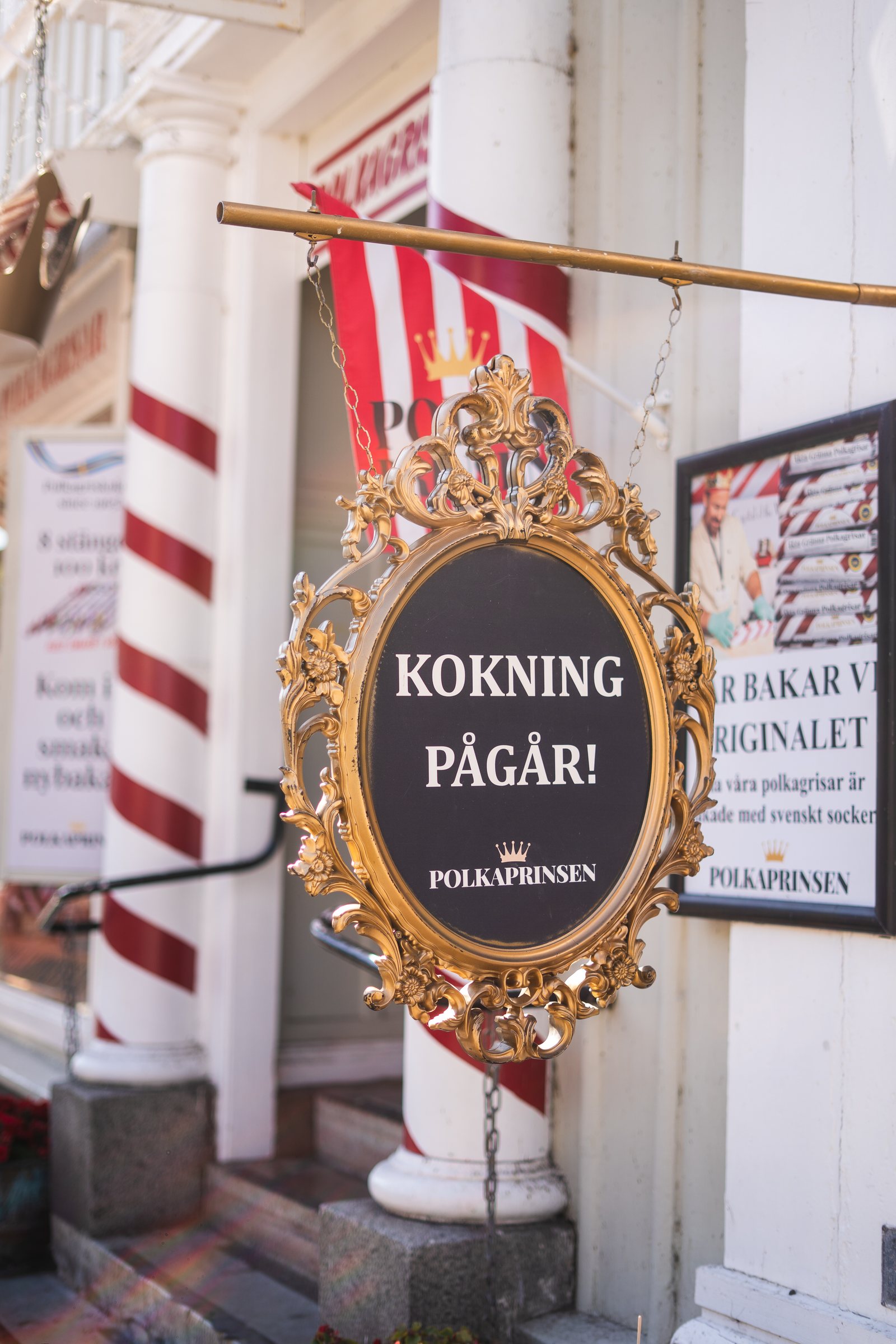Ornate 'Kokning pågår' sign outside a polkagris shop in Gränna