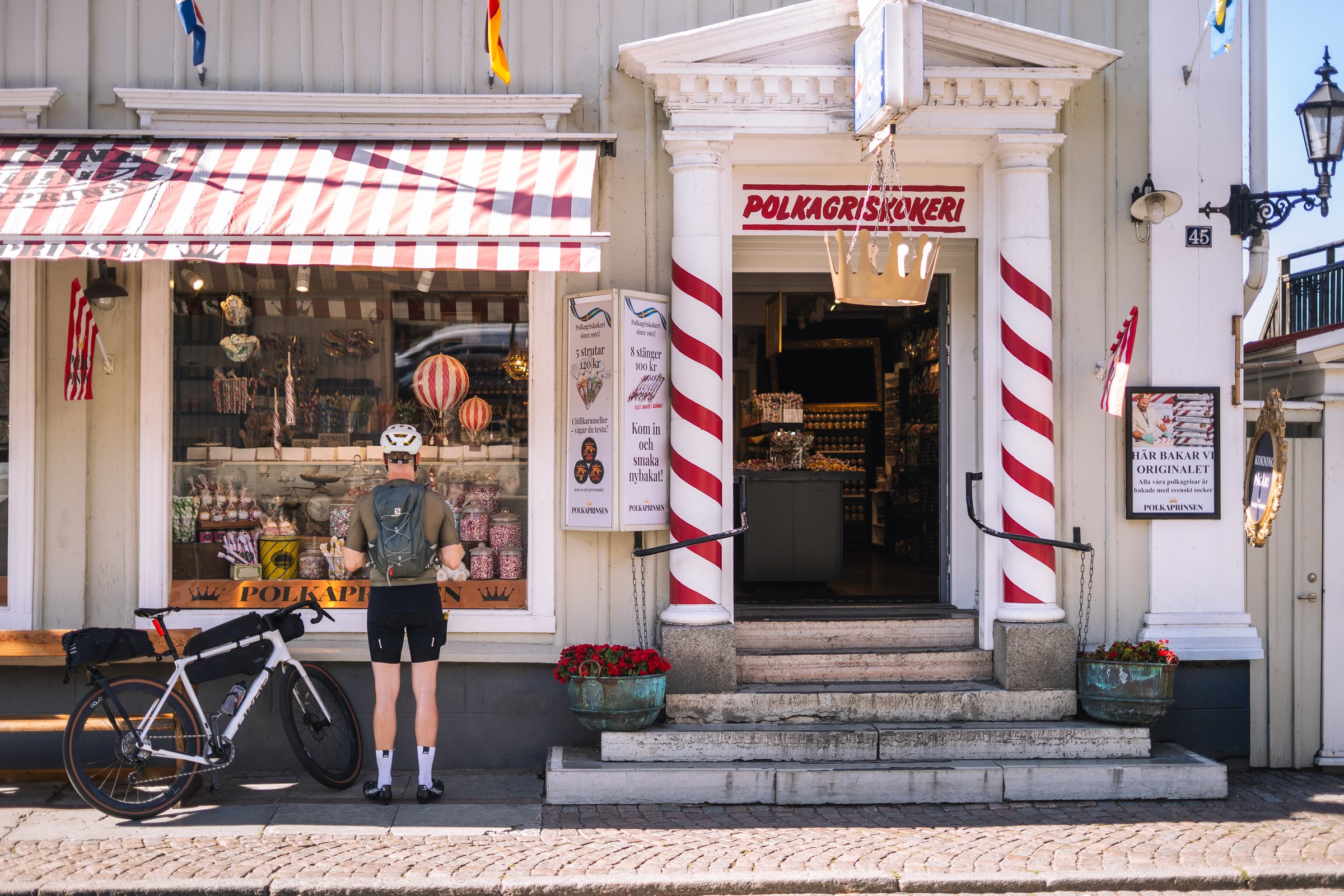 Cyclist outside a polkagris shop with striped awning in Gränna, bike leaning by the window