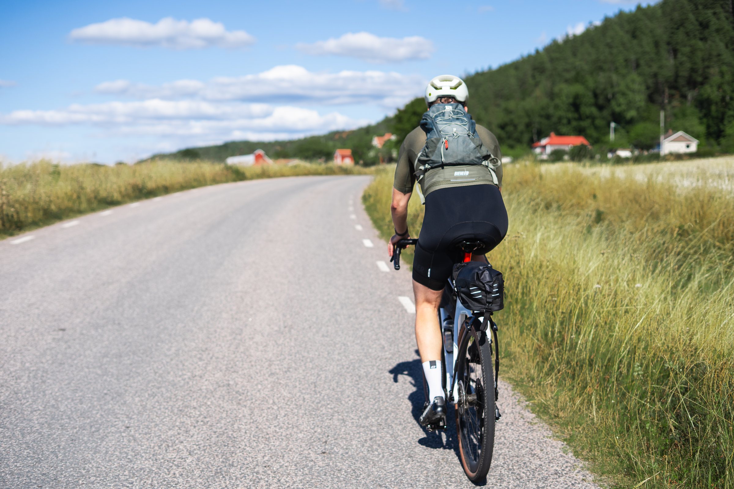 Cyclist riding a quiet road through tall grass towards wooded hills