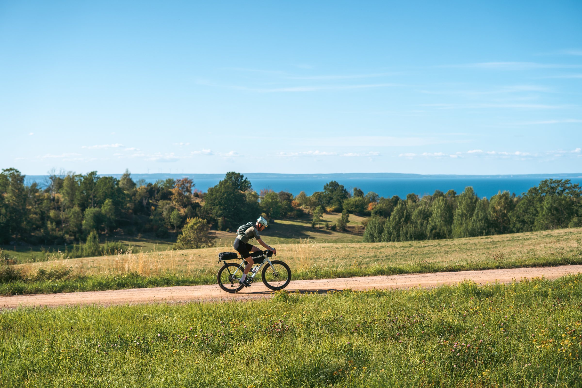 Cyclist on a gravel road through green fields with Lake Vättern behind