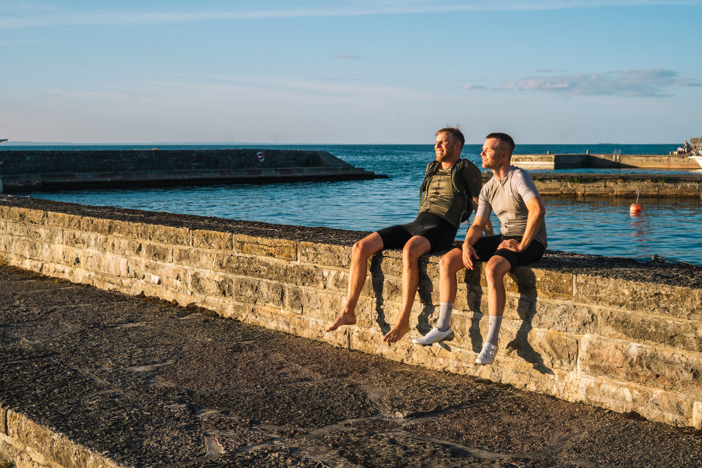 Two cyclists sitting barefoot on the harbour wall in Borghamn in evening sun