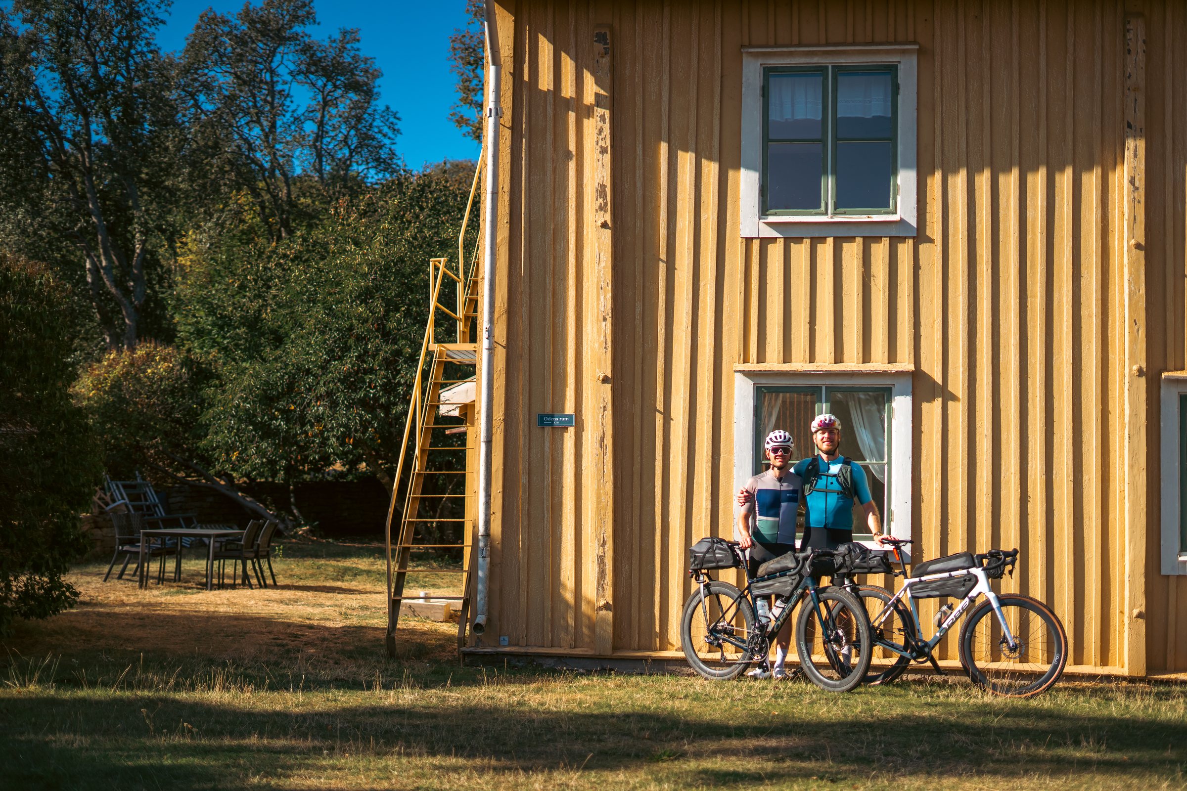 Two cyclists with their bikes outside a yellow wooden house in Borghamn