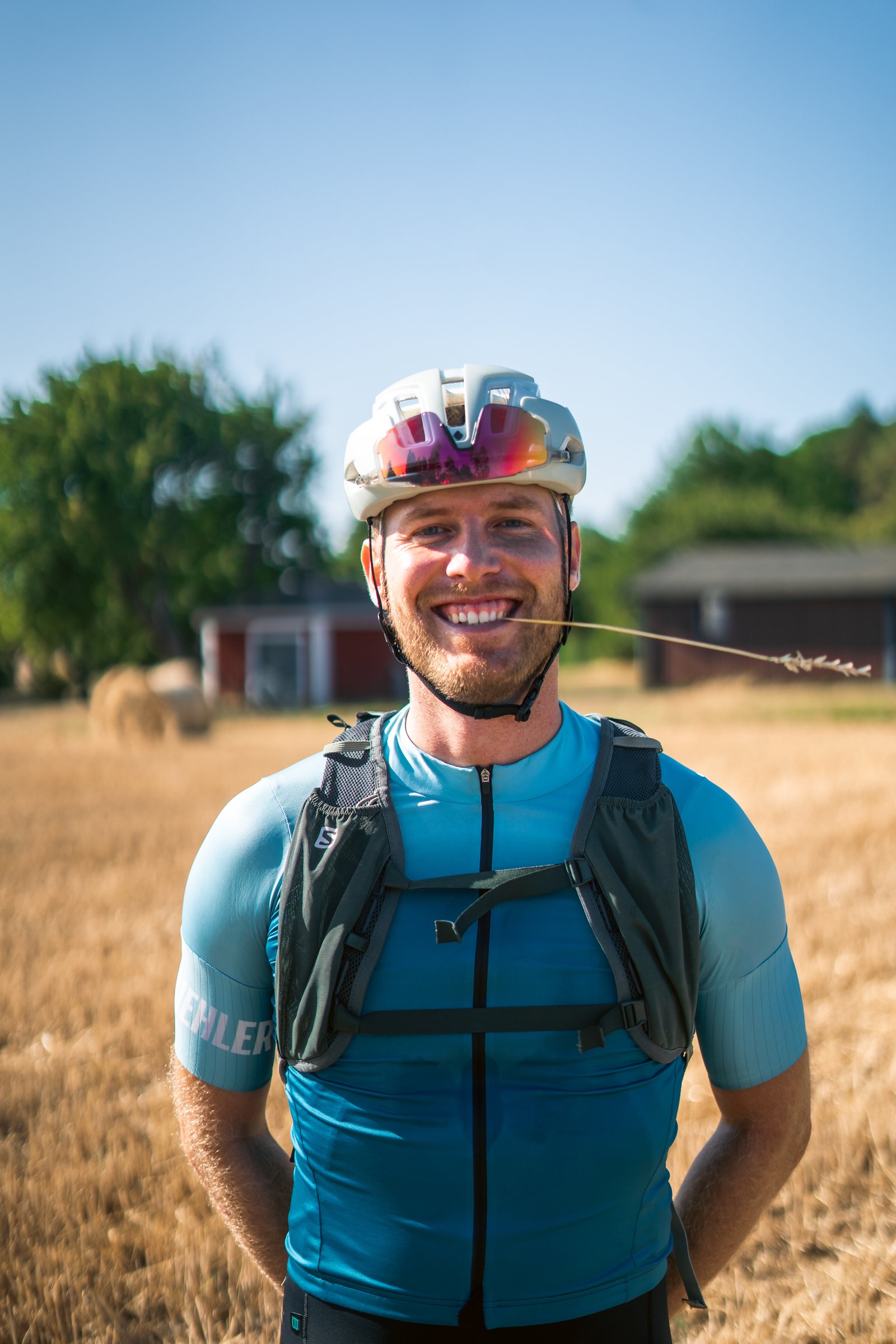 Smiling cyclist with a hydration vest in front of a harvested field