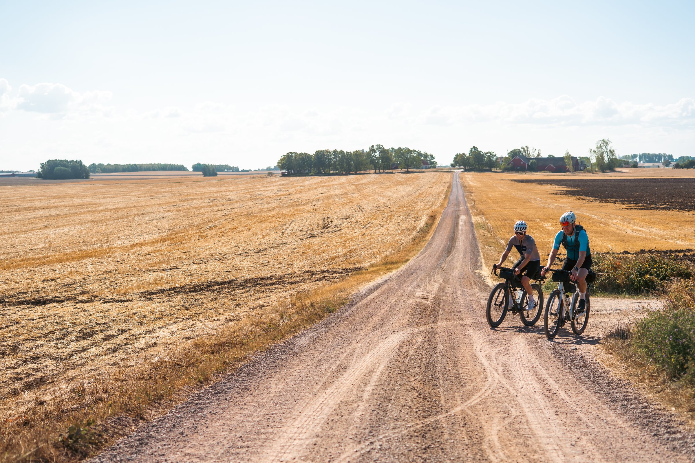 Two cyclists on a straight gravel road through stubble fields