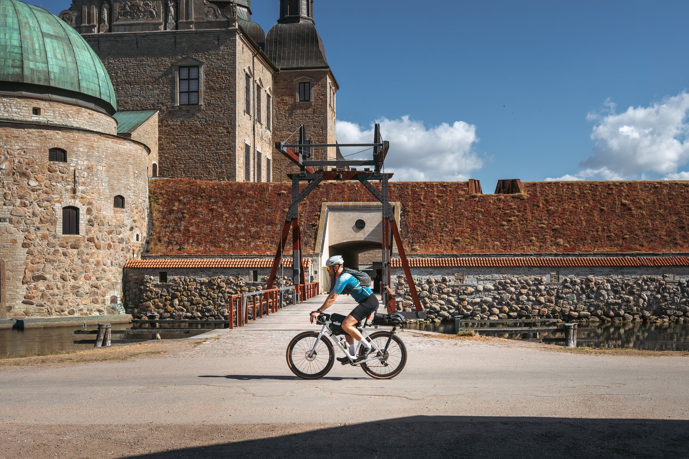 Cyclist riding past Vadstena castle and its moat bridge