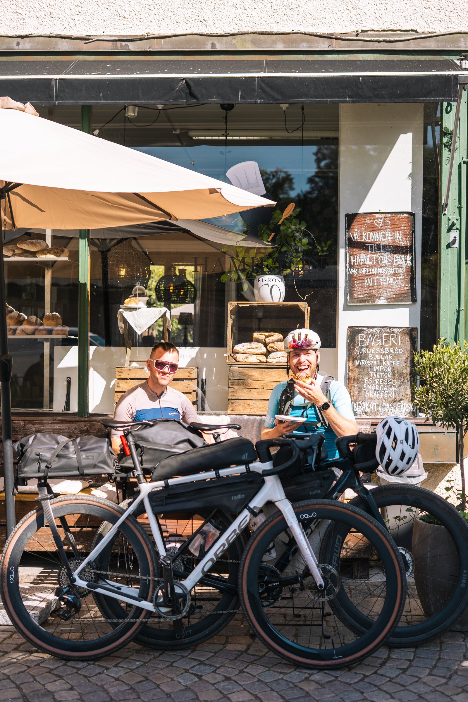 Two cyclists at a café table in Vadstena with their bikes parked in front