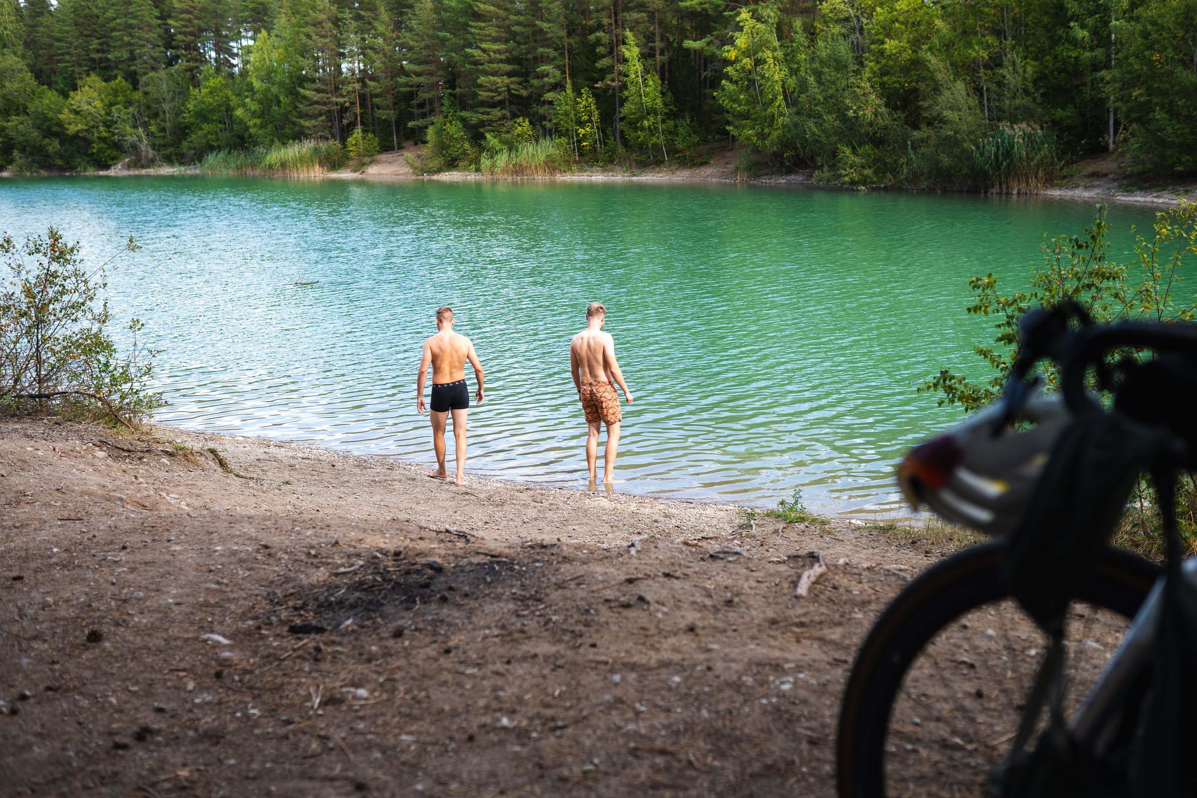 Two people wading into a turquoise lagoon surrounded by forest