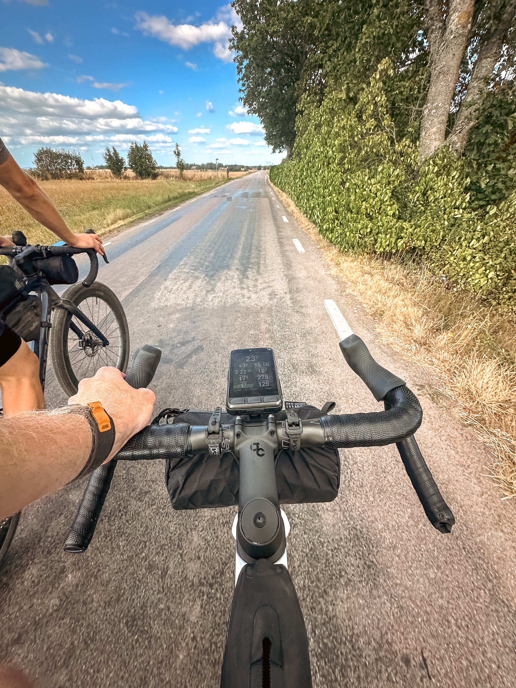 Riding a quiet asphalt road beside another cyclist, seen over the handlebars